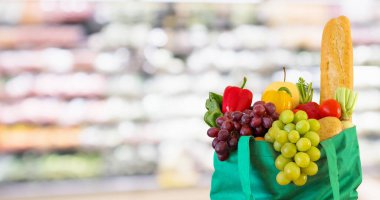 Yeniden kullanılabilir yeşil alışveriş poşetinde taze meyve ve sebzeler süpermarkette bulanık arka planda bokeh ışığı ile bulanık