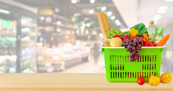 Shopping basket filled with fruits and vegetables on wood table with supermarket grocery store blurred defocused background with bokeh light