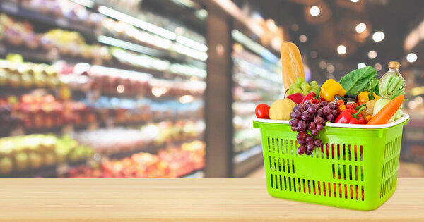 Shopping basket filled with fruits and vegetables on wood table with supermarket grocery store blurred defocused background with bokeh light