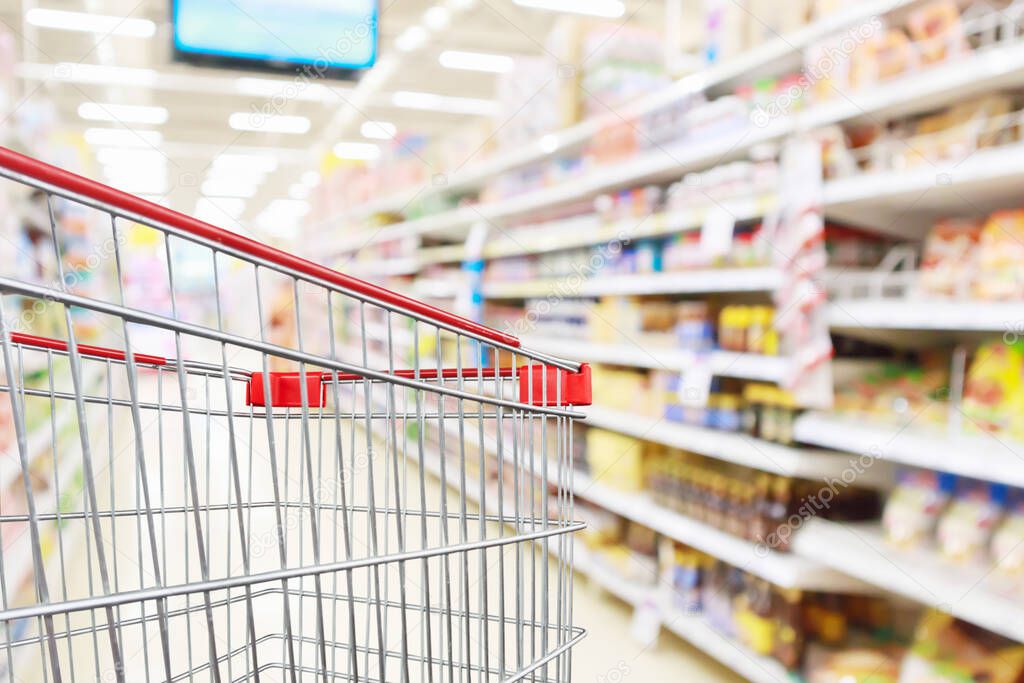 Empty shopping cart with abstract blur supermarket discount store aisle and product shelves interior defocused background