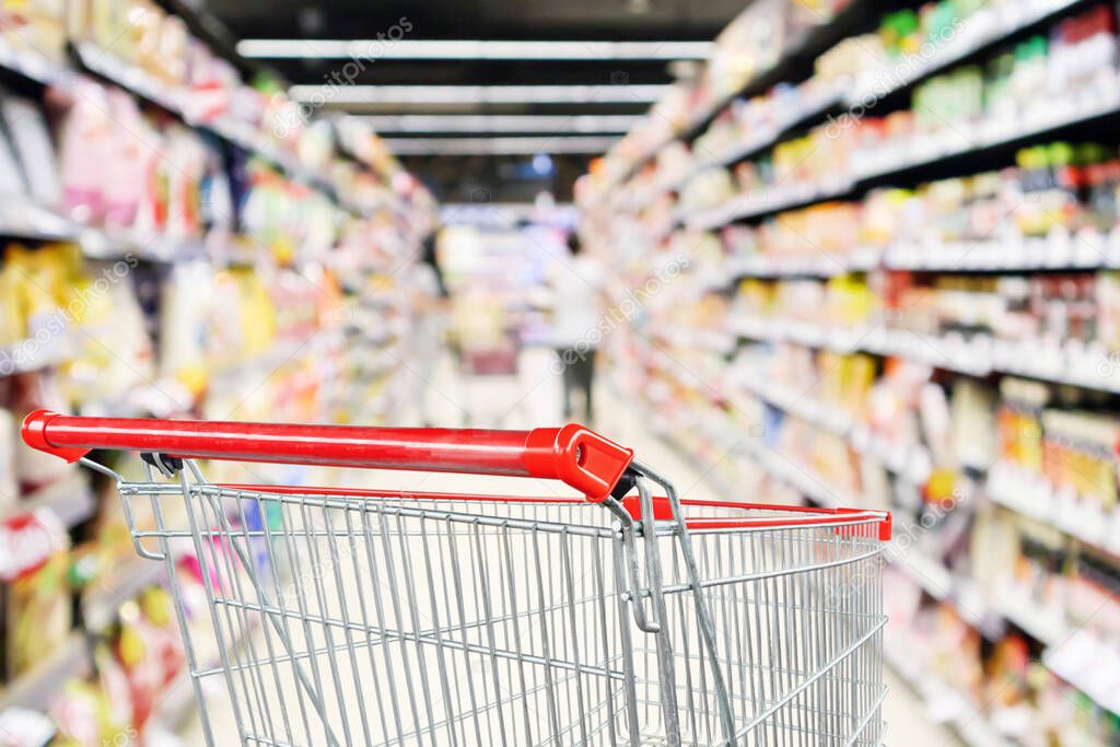 Empty shopping cart with abstract blur supermarket discount store aisle and product shelves interior defocused background