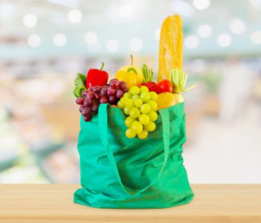 Yeniden kullanılabilir yeşil alışveriş poşetinde taze meyve ve sebzeler ahşap masanın üstünde süpermarket bakkalının bokeh ışıklı bulanık arka planıyla