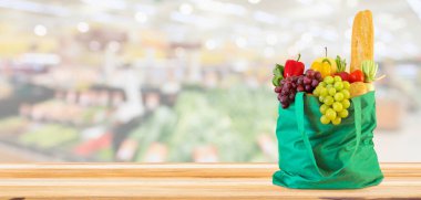 Yeniden kullanılabilir yeşil alışveriş poşetinde taze meyve ve sebzeler ahşap masanın üstünde süpermarket bakkalının bokeh ışıklı bulanık arka planıyla