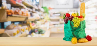 Yeniden kullanılabilir yeşil alışveriş poşetinde taze meyve ve sebzeler ahşap masanın üstünde süpermarket bakkalının bokeh ışıklı bulanık arka planıyla