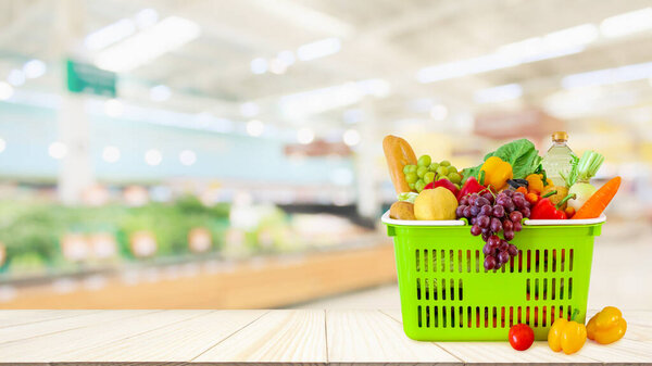 Shopping basket filled with fruits and vegetables on wood table with supermarket grocery store blurred defocused background with bokeh light