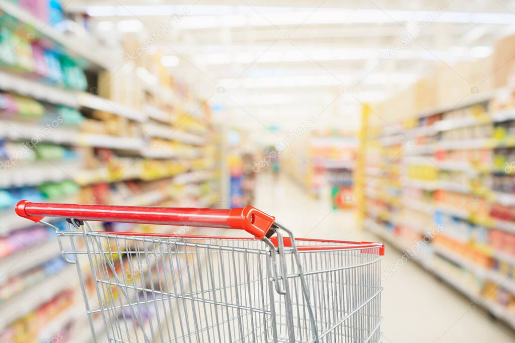 Supermarket aisle blurred background with empty red shopping cart