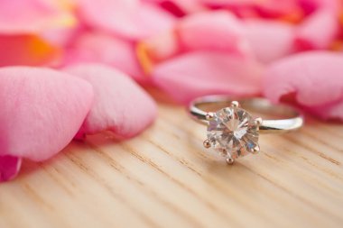Mücevher elmas yüzük ahşap masanın üzerinde. Güzel pembe gül yaprakları var. Yakın plan.