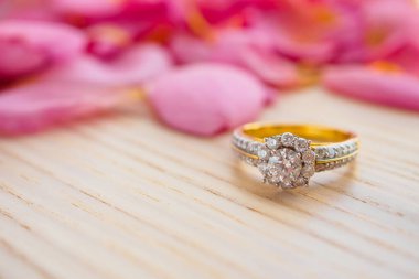 Mücevher elmas yüzük ahşap masanın üzerinde. Güzel pembe gül yaprakları var. Yakın plan.
