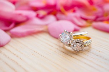 Mücevher elmas alyans ahşap masanın üstünde. Güzel pembe yapraklı arka planda. Yakın plan.