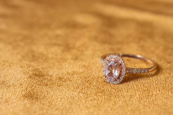 Jewelry pink diamond ring on golden fabric background close up