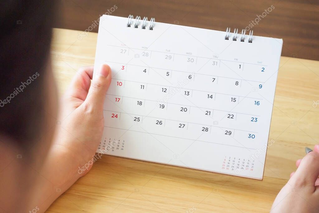 calendar page with female hand holding pen on desk table