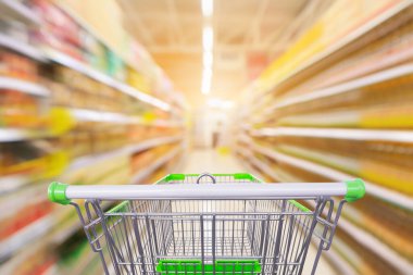 Market koridoru olan boş yeşil alışveriş arabası baharat ve sebze yağı şişeleri, ürün rafları iç taraf bulanık arka plan.