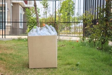 Kahverengi çöp kutusundaki plastik şişeler yeşil çimlerin üzerinde