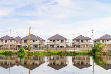 Yeni ev binası yansıması gölde suyla birlikte bulutlu ve mavi gökyüzü olan konut inşaat sahasında.