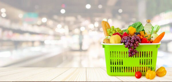 Shopping basket filled with fruits and vegetables on wood table with supermarket grocery store blurred defocused background with bokeh light