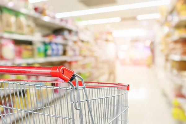 Empty shopping cart with abstract blur supermarket discount store aisle and product shelves interior defocused background