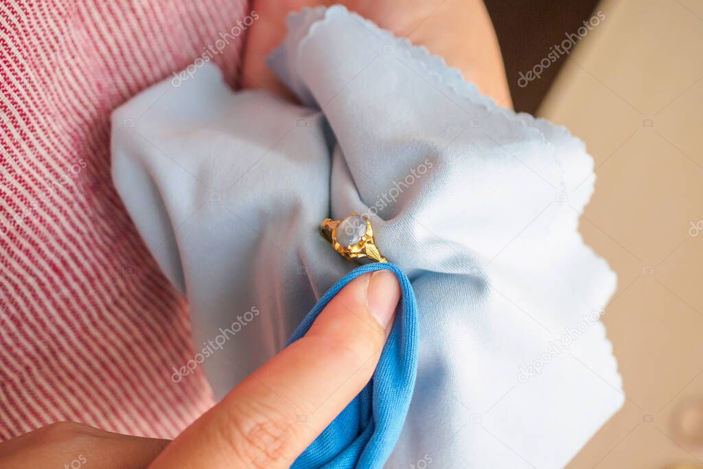 Jeweller hand polishing and cleaning gold jewelry ring with micro fiber fabric