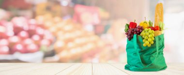 Yeniden kullanılabilir yeşil alışveriş poşetinde taze meyve ve sebzeler ahşap masanın üstünde süpermarket bakkalının bokeh ışıklı bulanık arka planıyla