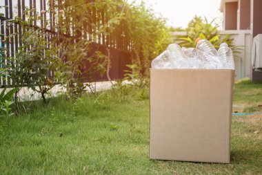 Kahverengi çöp kutusundaki plastik şişeler yeşil çimlerin üzerinde