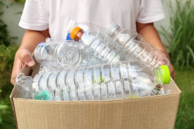Elinde kahverengi geri dönüşüm kutusuyla plastik şişeleri tutan.
