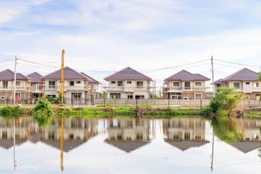 Yeni ev binası yansıması gölde suyla birlikte bulutlu ve mavi gökyüzü olan konut inşaat sahasında.