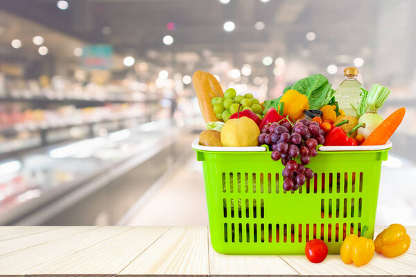 Shopping basket filled with fruits and vegetables on wood table with supermarket grocery store blurred defocused background with bokeh light