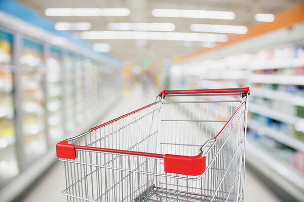 Supermarket aisle blur defocused background with empty red shopping cart