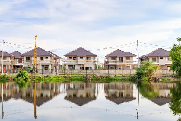 New house building reflection with water in lake at residential estate construction site with clouds and blue sky