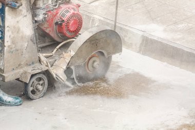 İnşaat alanında beton yol kesen elmas testeresi kullanan bir işçi.