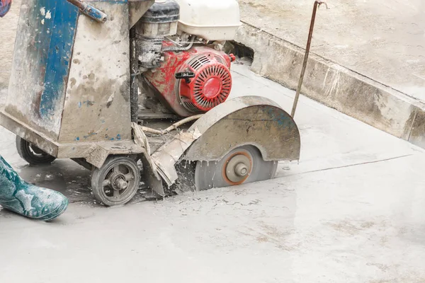 Worker using diamond saw blade machine cutting concrete road at construction site