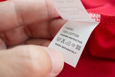 Beyaz çamaşırhanede el ele tutuşup kitap okuyoruz. Çamaşır yıkama talimatı. Kırmızı pamuklu gömleğin üzerindeki kıyafet etiketi.