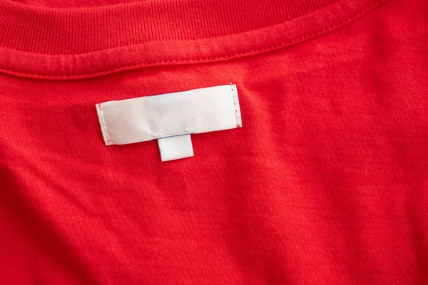 White blank clothing tag label on new red cotton shirt fabric texture background