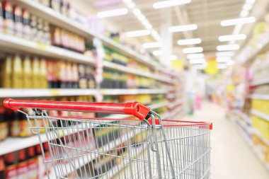 Soyut bulanık süpermarket indirim mağazası koridoru ve sos çeşnili ürün raflarıyla dolu boş alışveriş arabası.