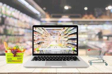 Süpermarket koridoru dizüstü bilgisayar ve alışveriş arabası ile bulanık arkaplan ahşap masa bakkalında online konsept