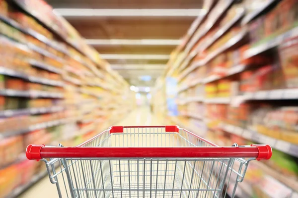 Empty red shopping cart with supermarket aisle interior with product shelves abstract blur background