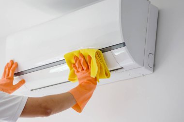 Asyalı adam mikrofiber bezle klimayı temizliyor.