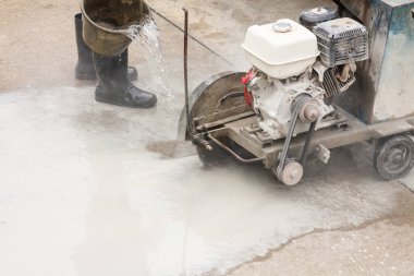İnşaat alanında beton yol kesen elmas testeresi kullanan bir işçi.