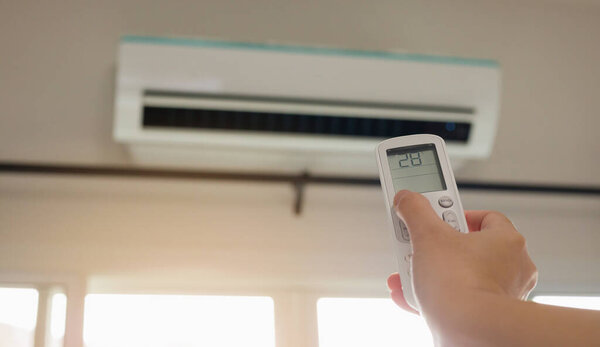 Рука с дистанционным управлением, направленная на кондиционер в помещении