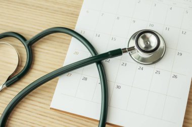 Ahşap masa arkası doktor randevu konseptinde takvim tarihli steteskop