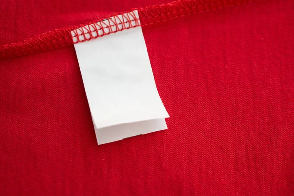 红色棉质衬衫上的白色洗衣店洗涤说明服装标签 — 图库照片