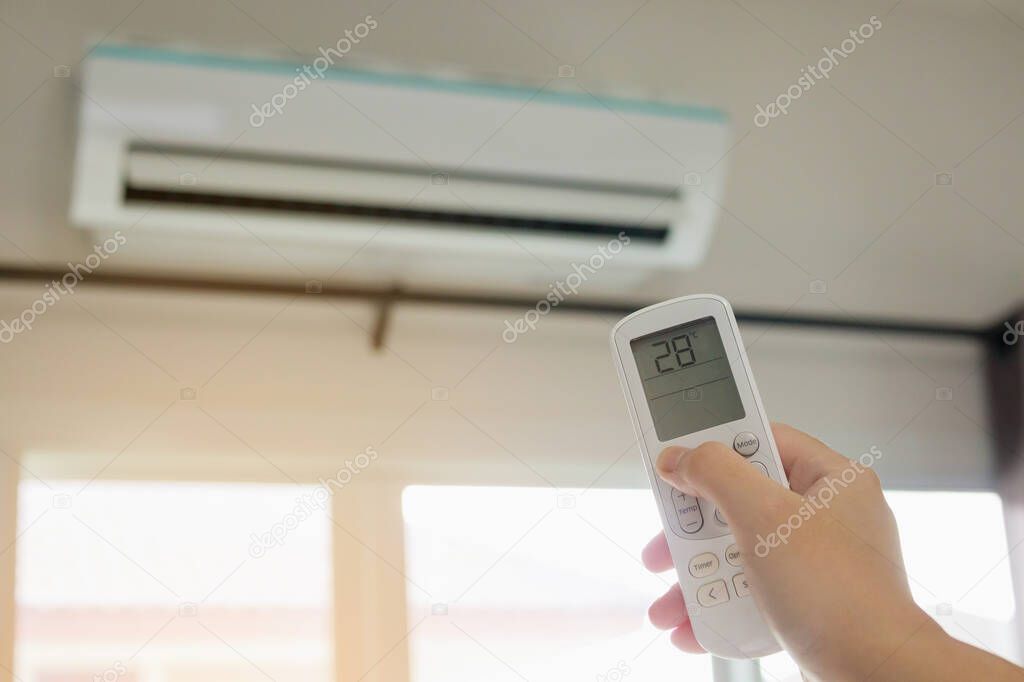 Hand with remote control directed on air conditioner inside the room