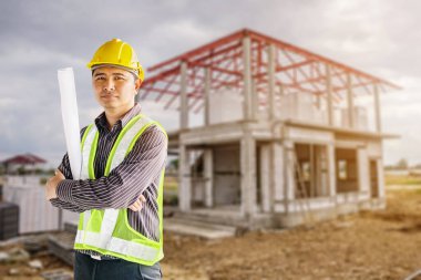 Asyalı işadamının portresi. İnşaat mühendisi. Koruyucu miğfer ve bina arka planında elinde planlar var.