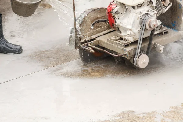 Worker using diamond saw blade machine cutting concrete road at construction site