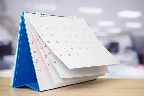 Calendar page flipping sheet on table with blurred office interior background business schedule planning appointment meeting concept