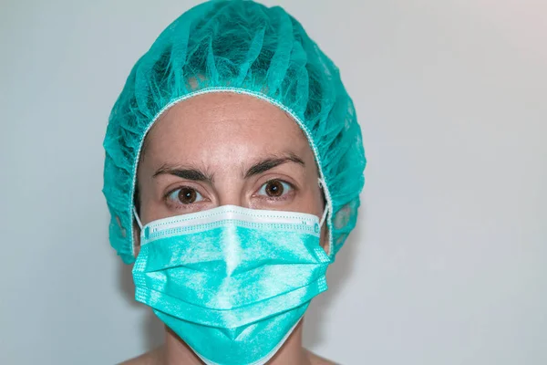 Tıbbi şapka ve maskeyle şokta olan genç bir hemşire. Koruma ve asistan.