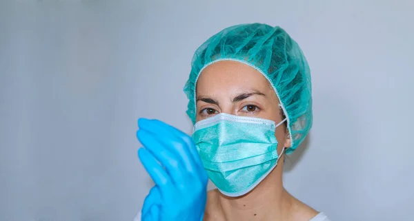 Genç bayan doktor hastanede koruma ekipmanlarıyla çalışmaya hazır. Plastik eldiven, maske ve tıbbi şapka.