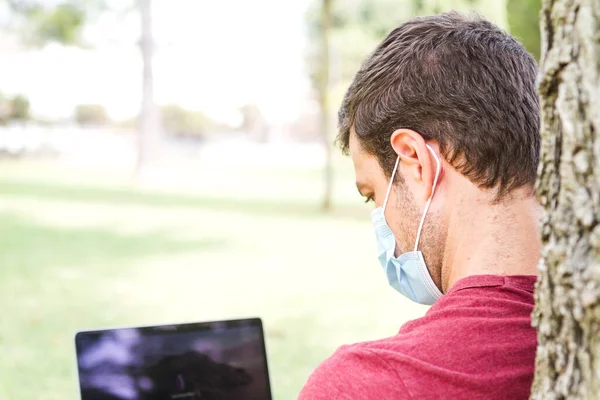 Yetişkinler parkta dizüstü bilgisayar ve koruyucu maskeyle seyahat ediyor. Bağımsız