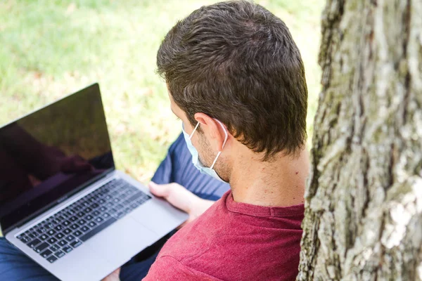 Yetişkinler parkta dizüstü bilgisayar ve koruyucu maskeyle seyahat ediyor. Serbest Çalışan