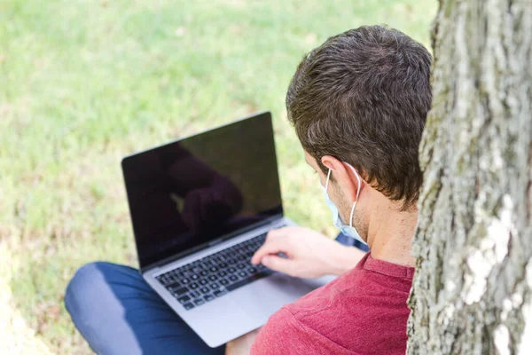 Yetişkinler parkta dizüstü bilgisayar ve koruyucu maskeyle seyahat ediyor. Serbest Çalışan