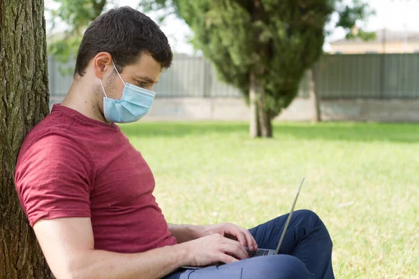 Yetişkinler parkta dizüstü bilgisayarla çalışıyor ve koruyucu maskeyle karşılaşıyorlar. Serbest Çalışan